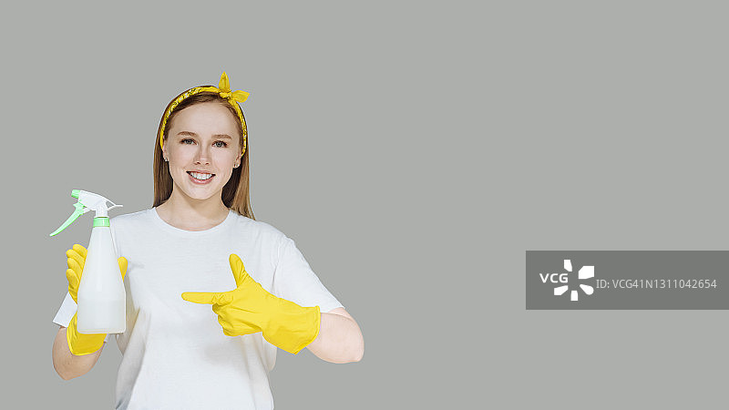 灰色背景下戴着黄色橡胶手套的年轻女孩，面带微笑的家庭主妇，家务清洁概念图片素材