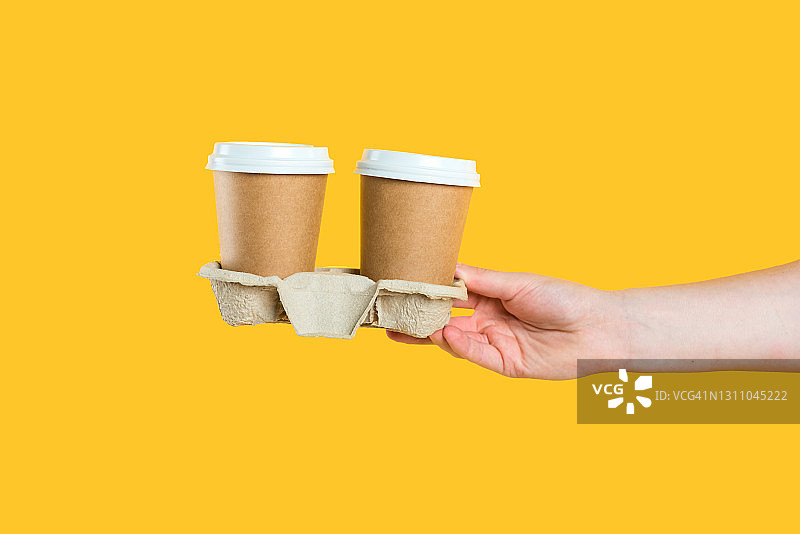 手持两杯牛皮纸咖啡，黄色背景图片素材