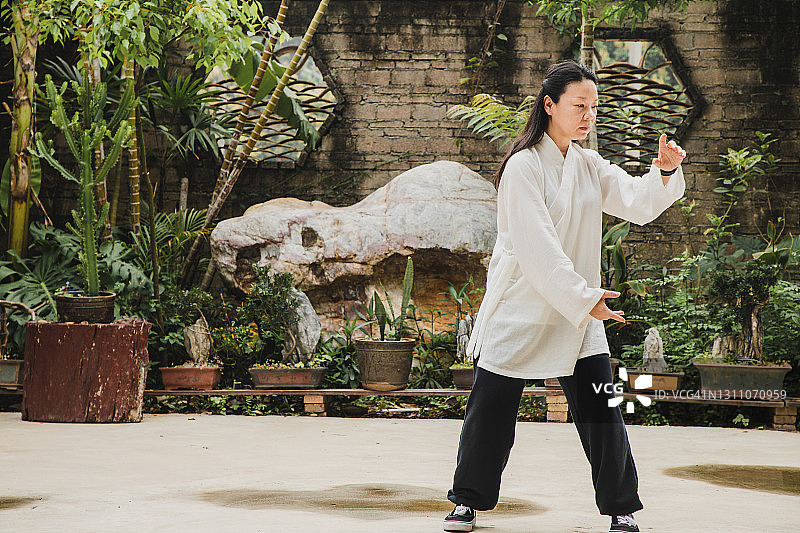 老年亚洲妇女在院子里练习太极拳图片素材