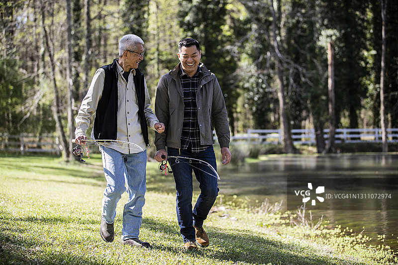 父亲和成年的儿子在农场湖边携带渔具散步图片素材