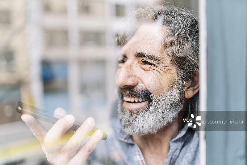 快乐的老年男人在家中窗边用手机交谈图片素材