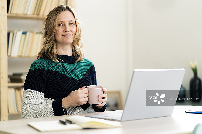 金发女人在家中拿着咖啡杯和笔记本电脑图片素材