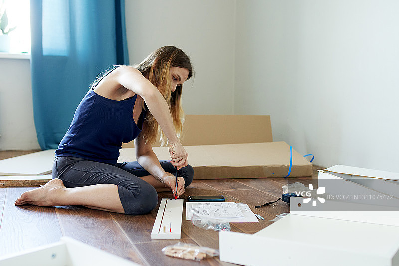 年轻女子参照说明书在公寓里组装带抽屉的新桌子图片素材
