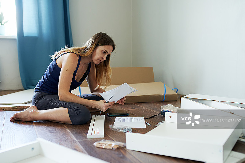 年轻女子参照说明书在公寓里组装带抽屉的新桌子图片素材