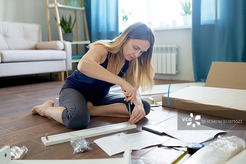 年轻女子参照说明书在公寓里组装带抽屉的新桌子图片素材
