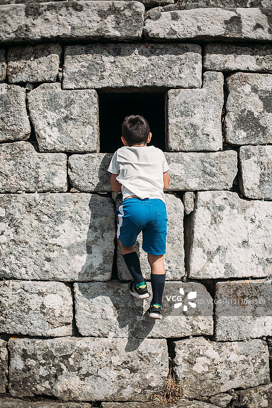 男孩坐在石墙上向窗外看图片素材