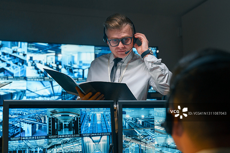 安保人员使用耳机实时接收重要信息，手中拿着打开的文件夹，里面也存储着必要的信息。图片素材