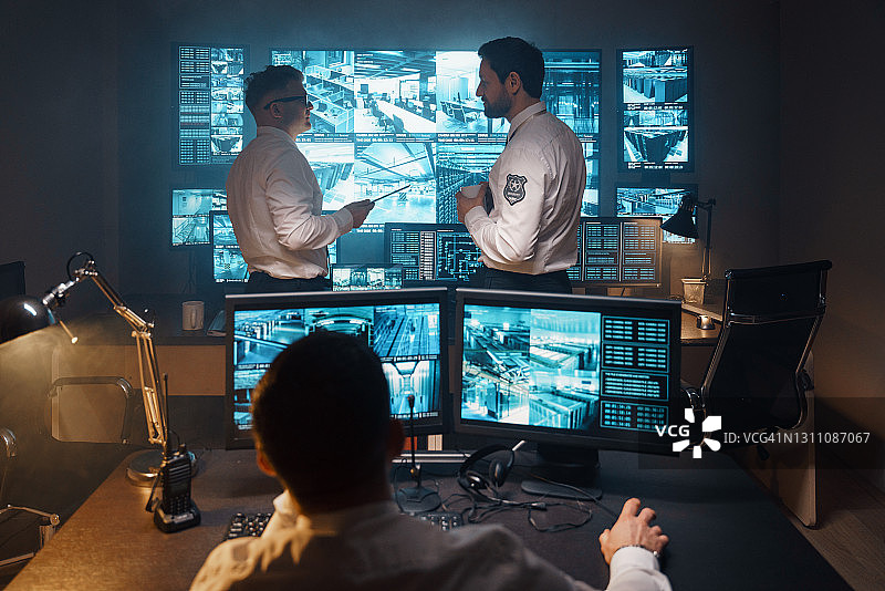 配备监控器和数字安全控制台的现代化高科技安保办公室里的安保人员图片素材