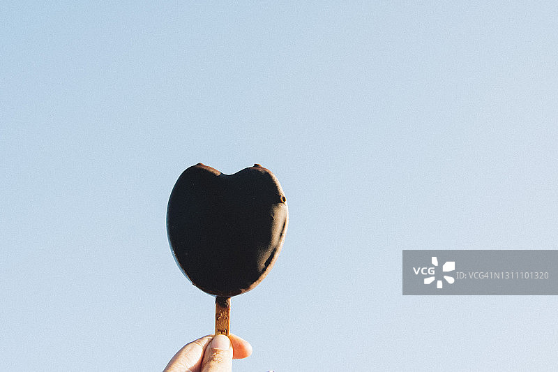 手持心形巧克力冰淇淋，夏日蓝天背景图片素材