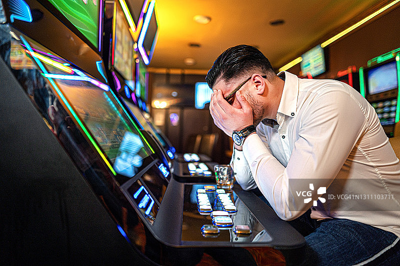 在赌场老虎机上输钱的焦虑男子图片素材