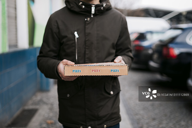 男人拿着外卖披萨在街上行走图片素材