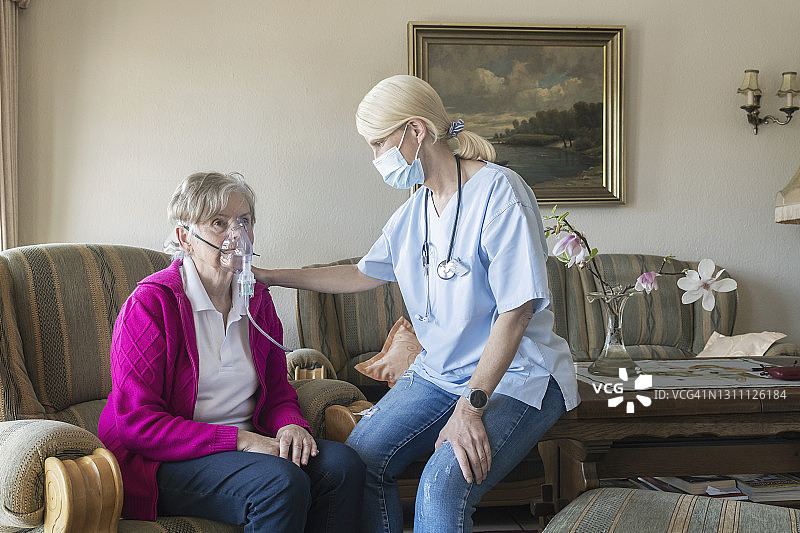 戴呼吸面罩的老年妇女，女护士正在帮助她图片素材