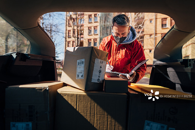 疫情期间使用非接触式配送方式，邮政人员在开始配送路线前，查看剪贴板上的配送时间表图片素材