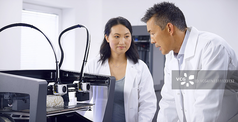 男女生物医学工程师在查看3D打印机时交谈图片素材