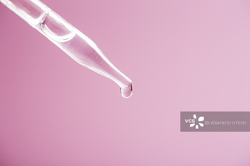 滴管滴落精华液气泡特写：浅粉色背景图片素材