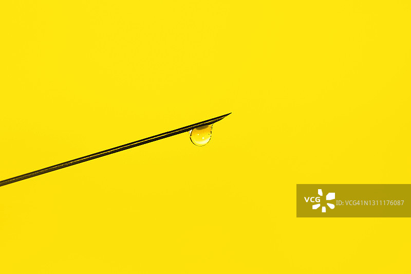 黄色背景下的注射器针头和透明药液滴落特写图片素材