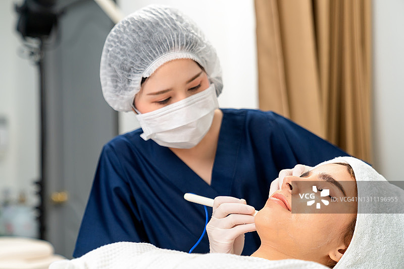 美容师在美容诊所为年轻女子清洁或去除面部角质图片素材