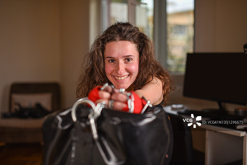 戴着拳击绷带，在室内对着拳击沙袋的年轻快乐的女拳击手画像图片素材