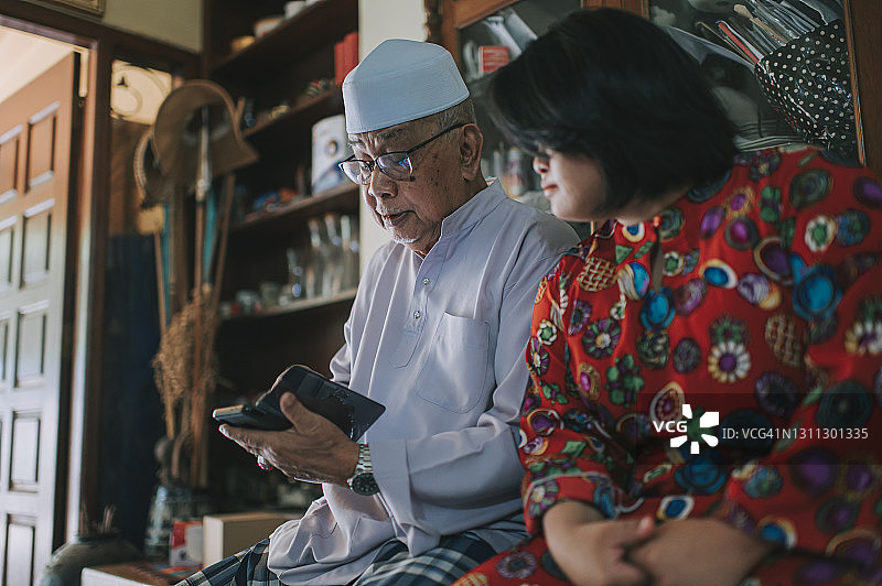 马来西亚爷爷在开斋节家庭聚会上看手机，孙女在他旁边图片素材