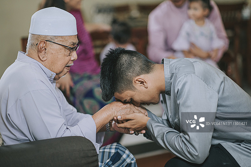 开斋节期间马来西亚穆斯林孙子在传统服装中向祖父道歉，马来西亚家庭在家庆祝开斋节图片素材