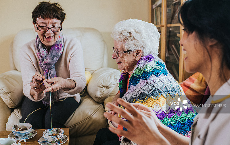 居家探访期间，女士在一位年长女性和护理人员旁编织图片素材
