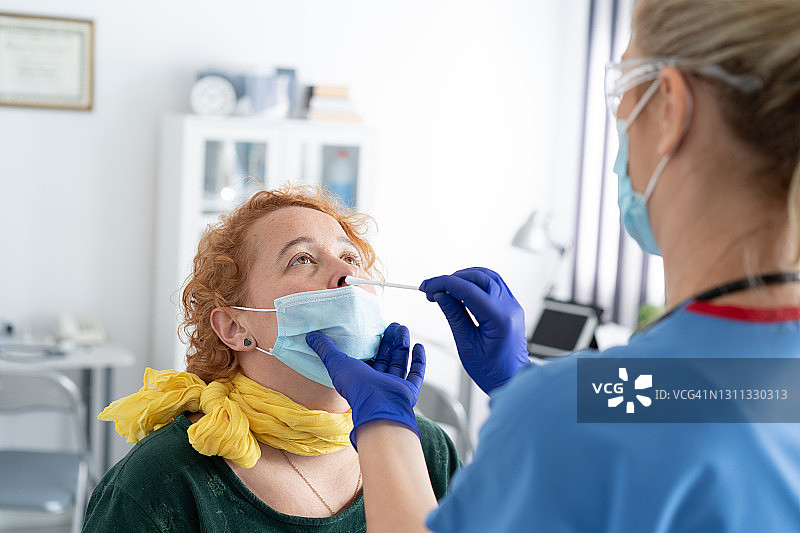 医生戴着防护口罩，从一名女性身上提取鼻拭子，以检测可能的新冠病毒感染图片素材
