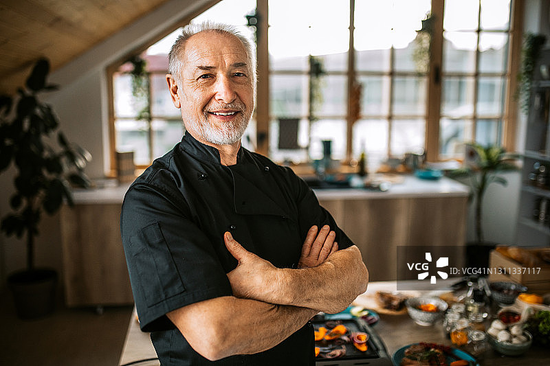 双臂交叉站在厨房里的老年厨师肖像图片素材