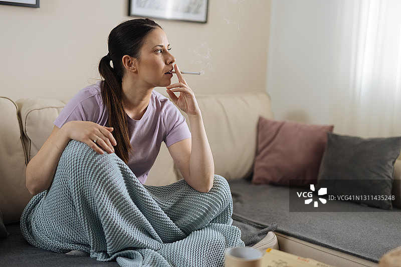 中年女人坐在毯子下抽烟图片素材