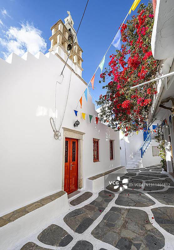 希腊米科诺斯岛乔拉镇的小巷，有白色希腊正教教堂和红色九重葛图片素材