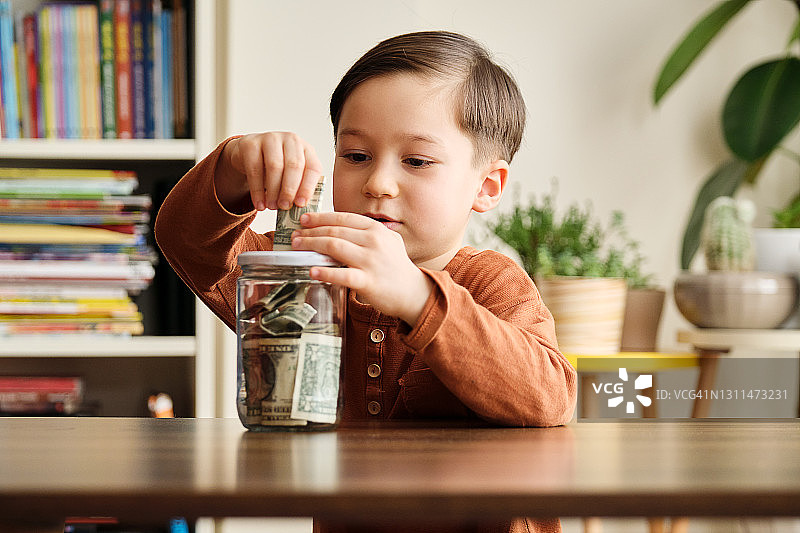 孩子在家中玻璃罐里存钱图片素材