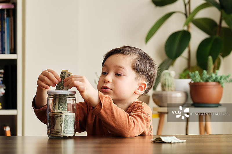 孩子在家中玻璃罐里存钱图片素材
