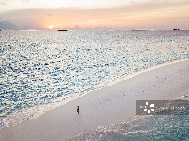 年轻女子站在马尔代夫碧绿的海水中的沙洲上，沐浴日落图片素材