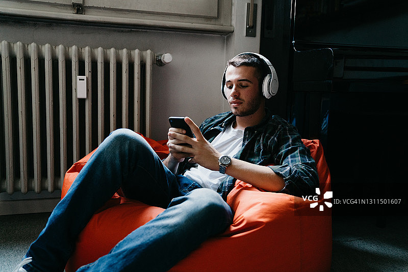 年轻男子在卧室里发短信和听音乐。图片素材