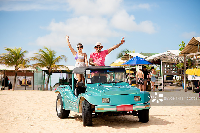 站在沙滩车后方挥手的微笑情侣图片素材