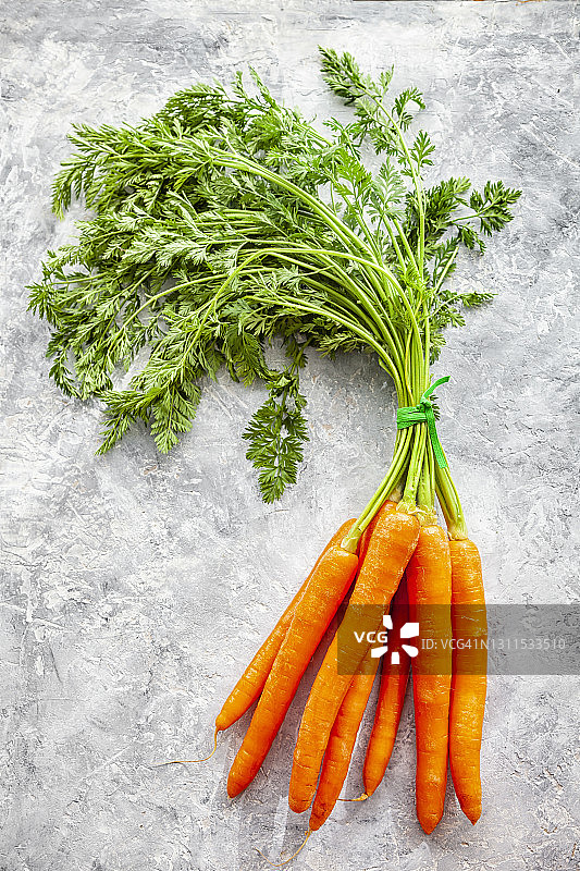 混凝土背景上，带绿叶的新鲜胡萝卜的俯视图图片素材