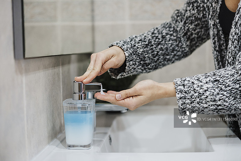 女人在浴室的水槽旁将洗手液喷在手上图片素材