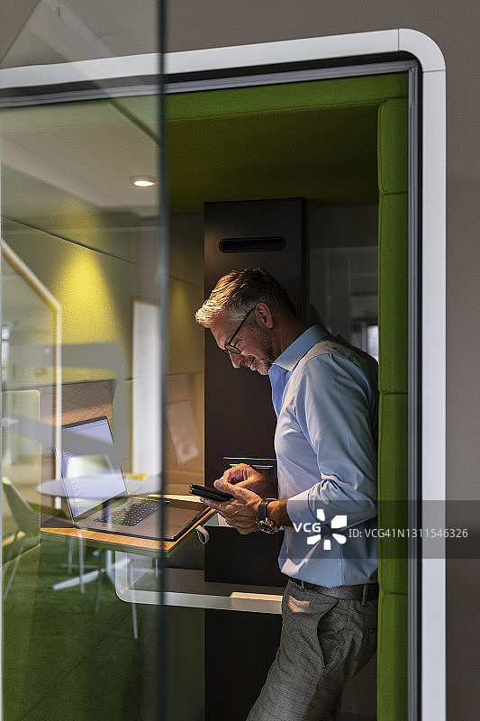 中年商人站在办公室的隔音间里使用手机图片素材
