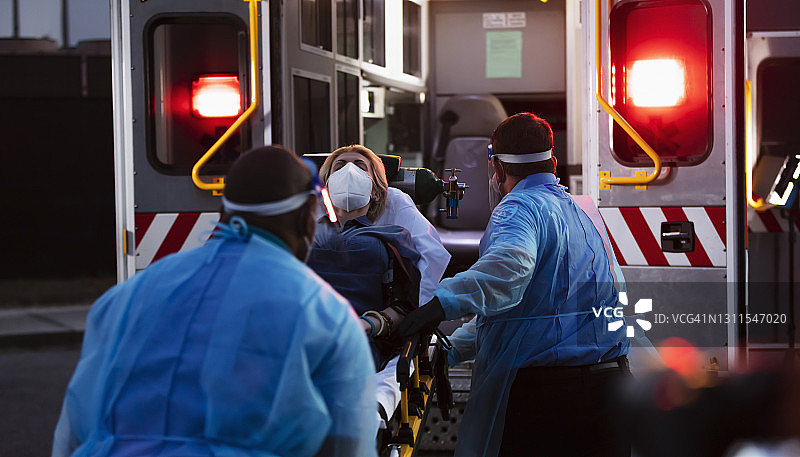 救护人员将病人抬上救护车，身穿防护装备图片素材