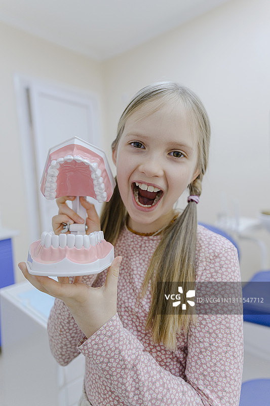 站在牙医诊所，手里拿着假牙的金发小女孩肖像图片素材