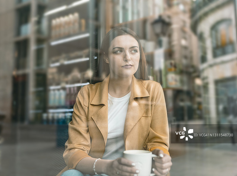 隔着玻璃窗拍摄的坐在咖啡馆里的年轻女子图片素材