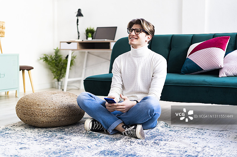 快乐的男人坐在客厅的地毯上，看向远方图片素材