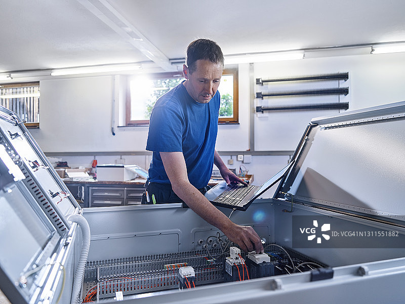 男电工在车间通过笔记本电脑检查电源图片素材