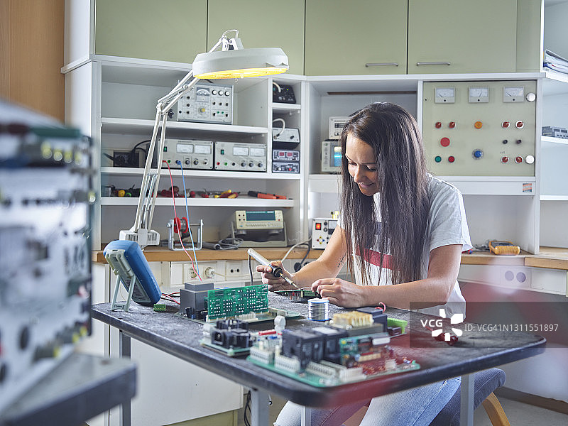 在电气车间用烙铁焊接电路的微笑女电工图片素材