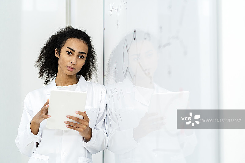 自信的女研究员在实验室里靠在白板上，手持平板电脑图片素材