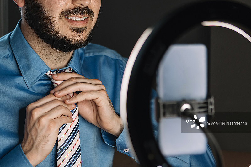 中年网红在工作室用手机拍摄vlog并调整领带图片素材