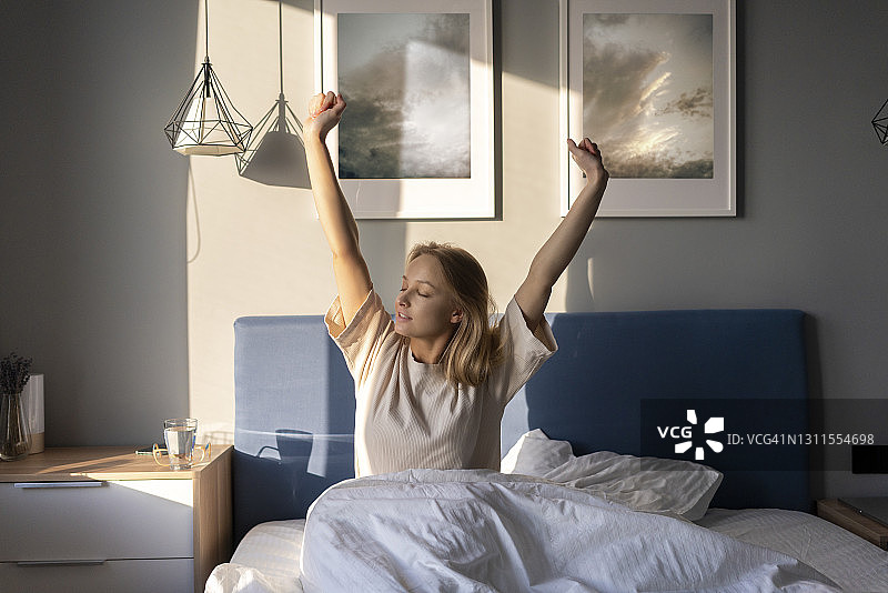 年轻女子在家中坐在床上伸展手臂图片素材