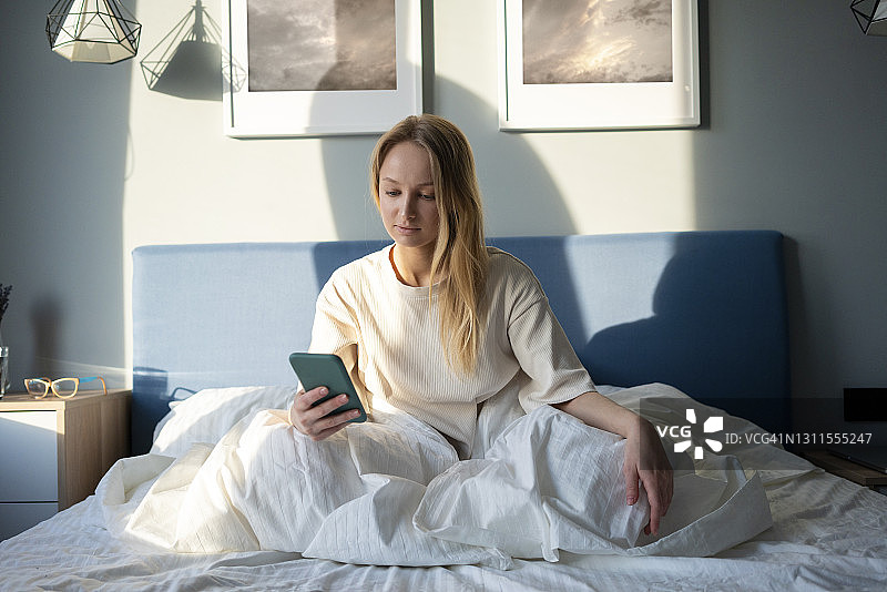 在家坐在床上玩手机的女人图片素材
