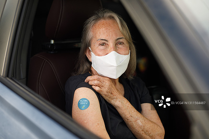 老年妇女展示她的新冠疫苗接种徽章图片素材