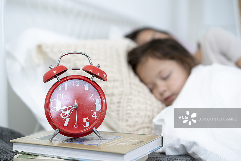 睡在白色床上的少女，前景是书堆上的闹钟图片素材