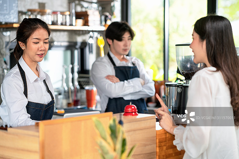 咖啡店里的年轻女咖啡师从顾客那里接单，年轻男咖啡师站在背景中图片素材